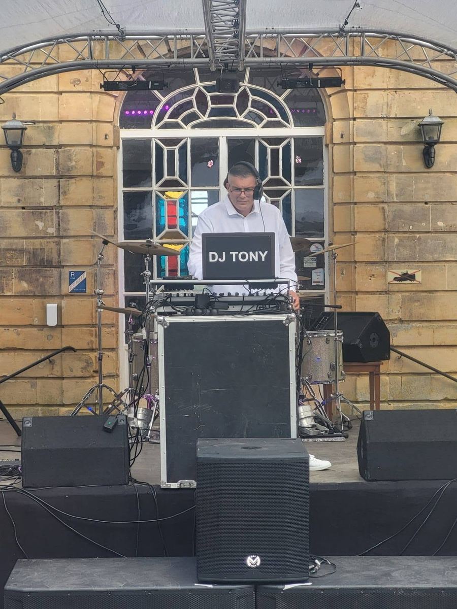 Tony au casque derrière son stand DJ Tony, devant un vitrail